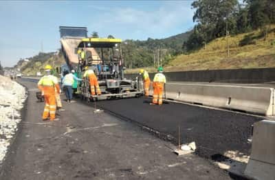 Equipe acompanhando a vibroacabadora na aplicação da camada asfáltica da faixa adicional, com tráfego separado por barreira de concreto